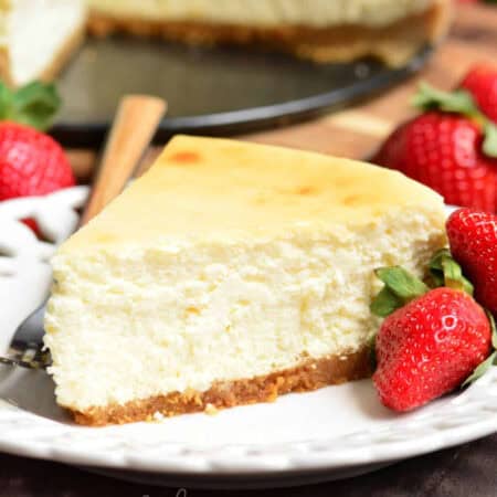 a slice of NY style cheesecake on the plate with strawberries around.