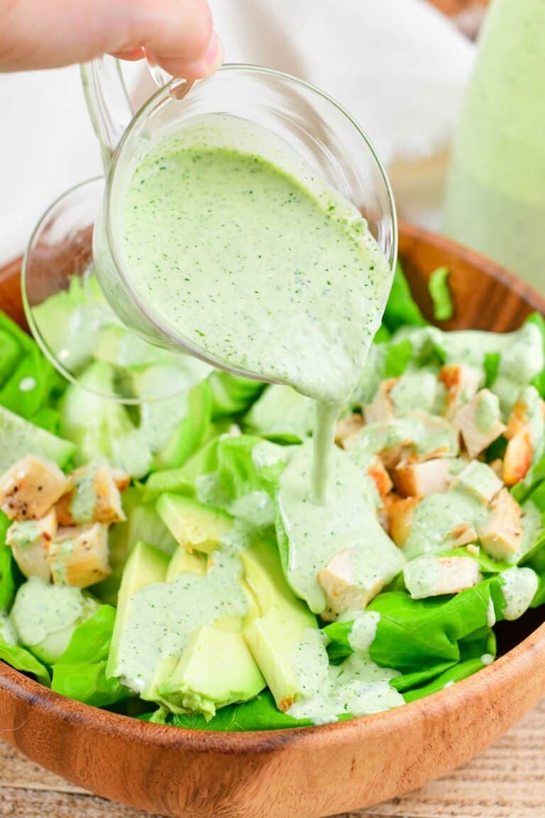 pouring the green goddess dressing over the salad in a bowl