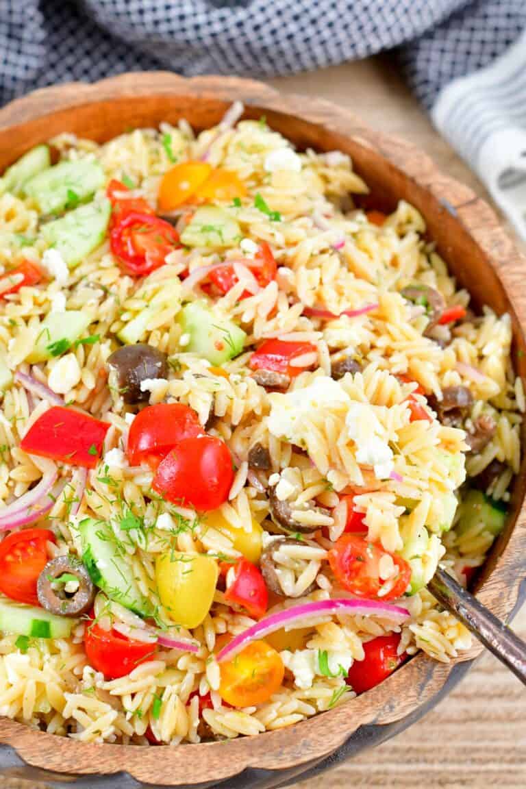 scooping out orzo salad from a wooden bowl