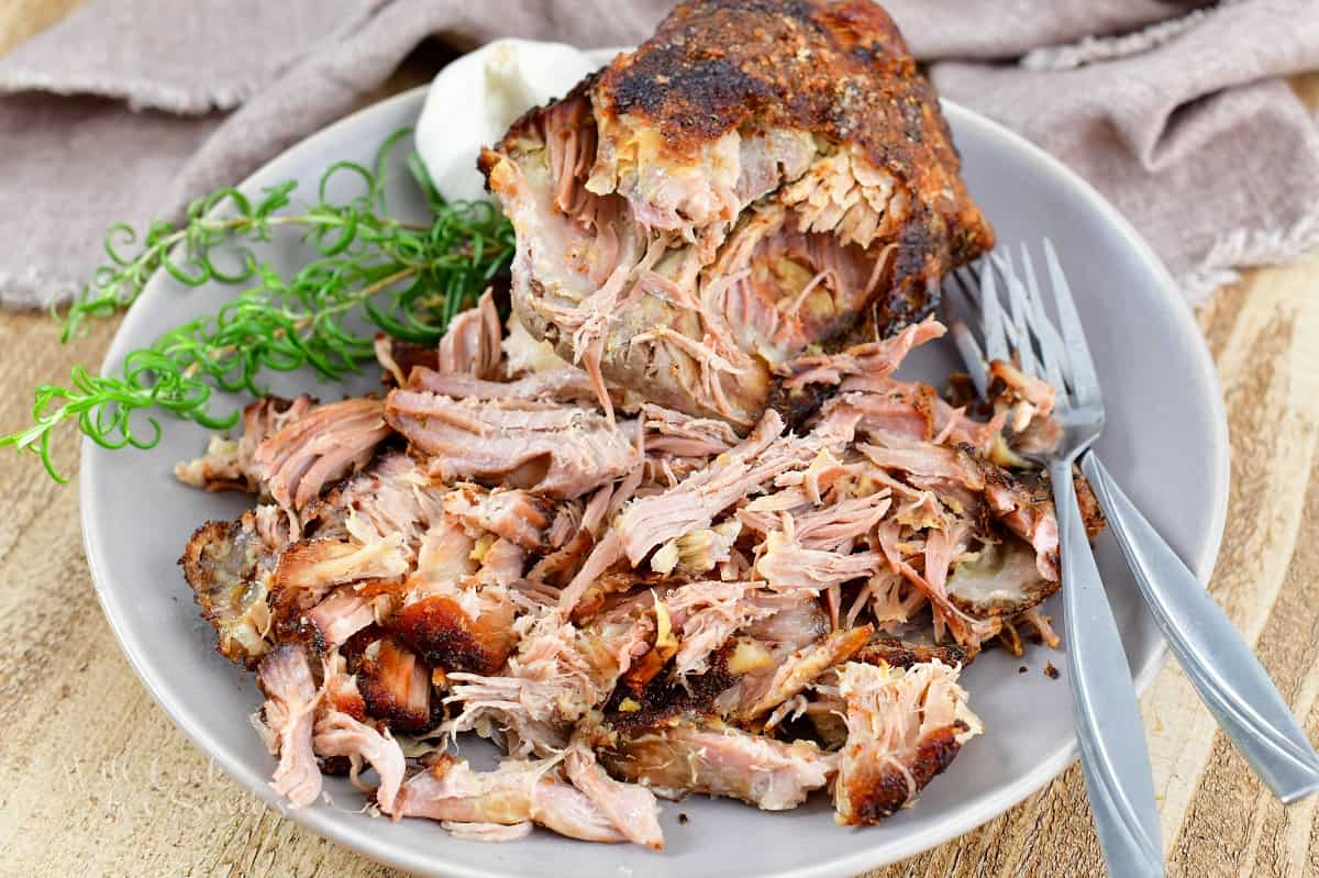 pulled pork on the plate with forks, garlic bulb and rosemary.