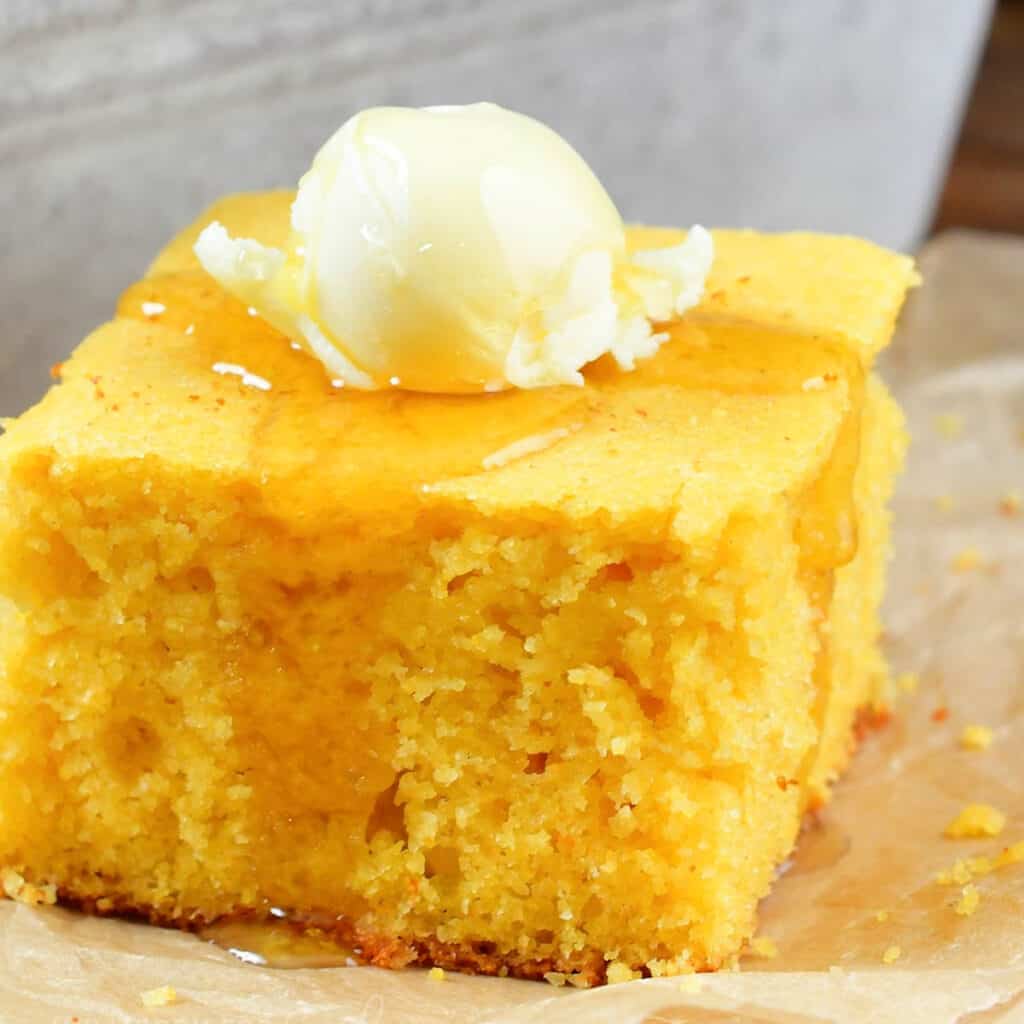 closeup square of cornbread with butter and honey.