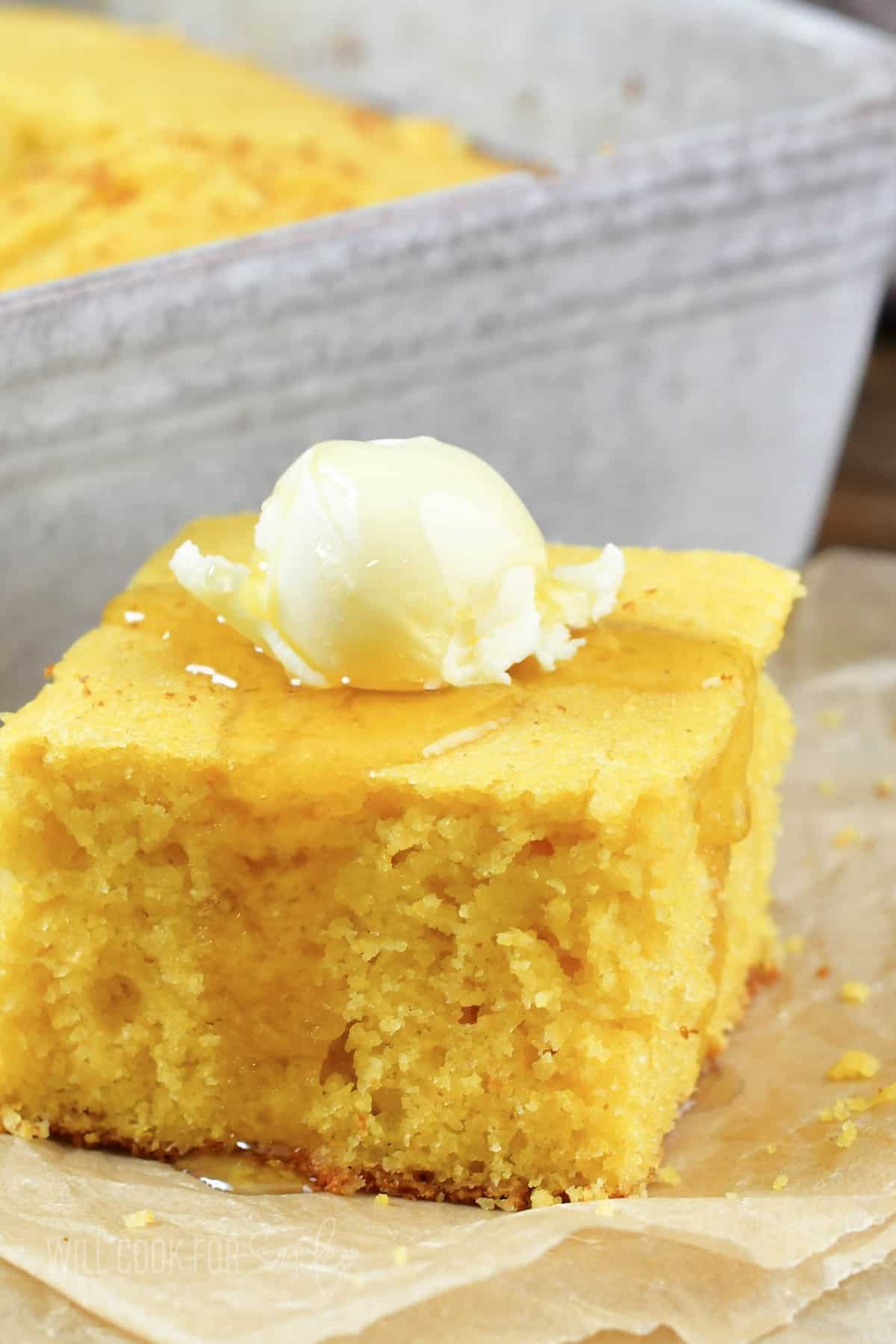 closeup of cornbread square topped with butter and honey.