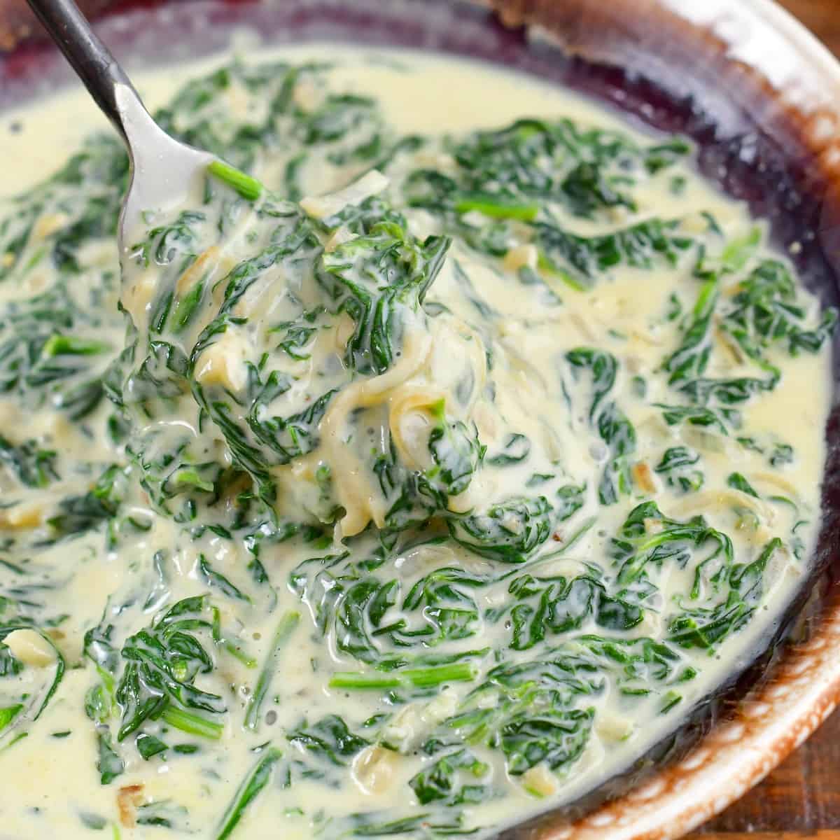 closeup squared image of scooping out creamed spinach.