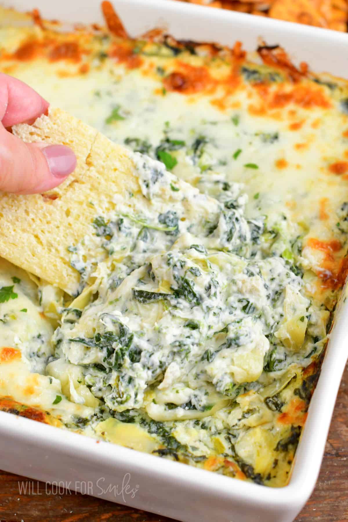 scooping out spinach dip from the baking dish.