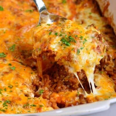 Scooping some cheesy casserole out of the white baking dish.