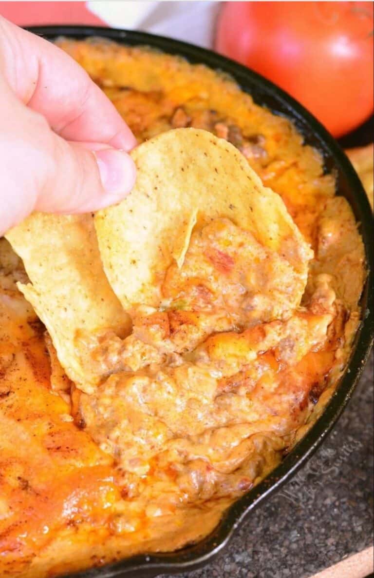 scooping some taco dip from the skillet with two round tortilla chips.