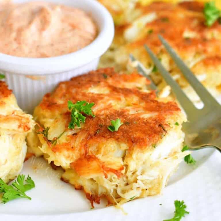 one crab cakes on a plate with a fork and pink sauce next to it.