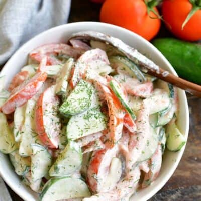 tomato cucumber salad mixed in a white bowl next to tomatoes on a vine.