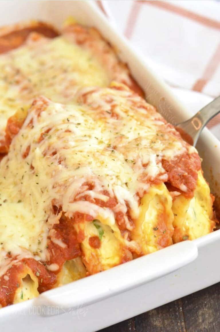 pulling out some manicotti from the white baking dish with a silver spatula.