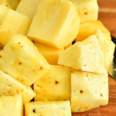 cup fresh pineapple chunks on a cutting board with part of a knife visible.