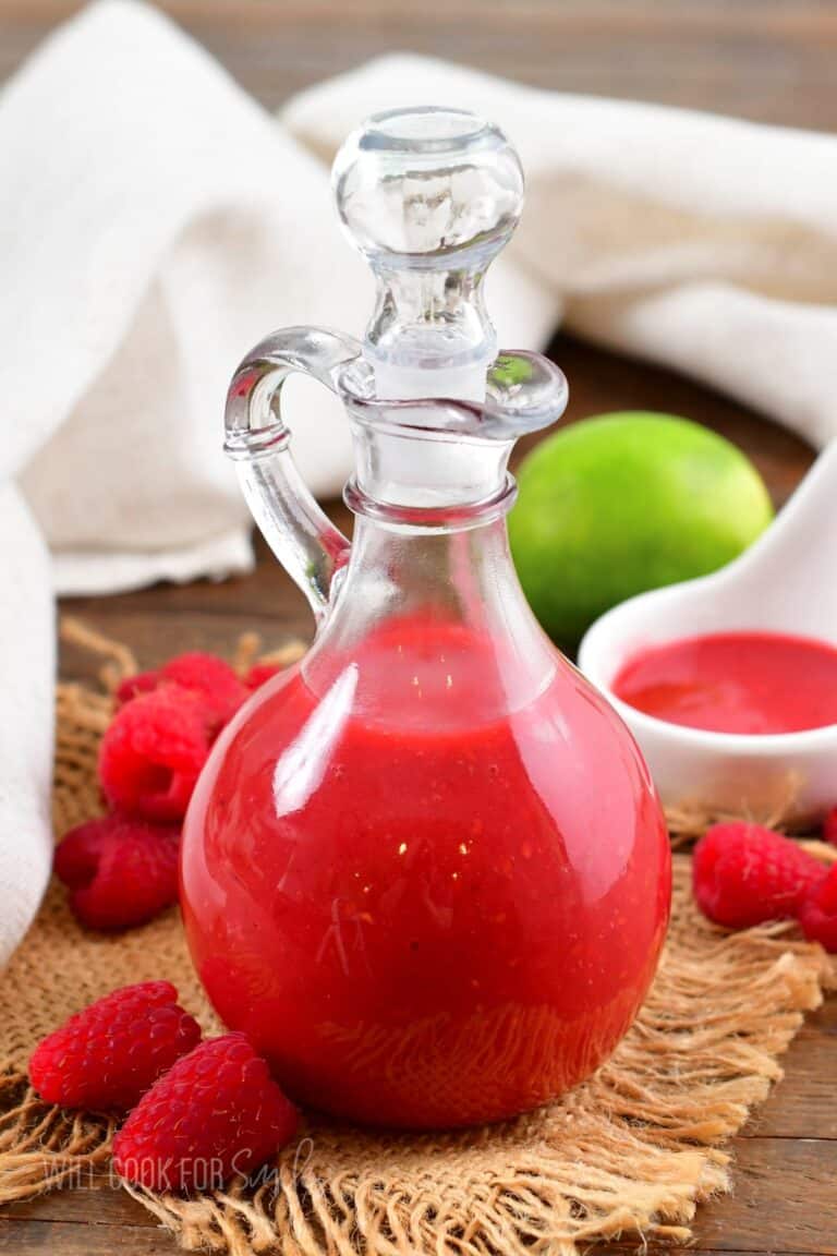 tall glass dressing jar with bright raspberry vinaigrette in it and berries around.