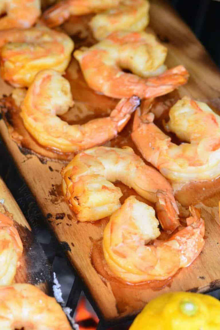 wooden plank with several shrimp on top and lemon on the grill.