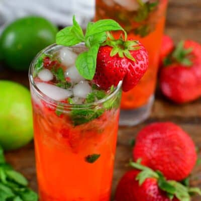 two glasses with bright strawberry mojito cocktails and berries around on the table.