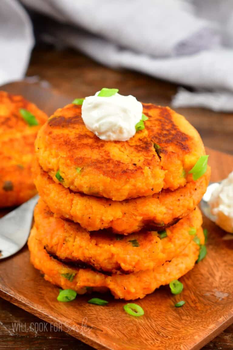 A stack of sweet potato cakes on a cutting board with a dollop of sour cream on top with green onions.