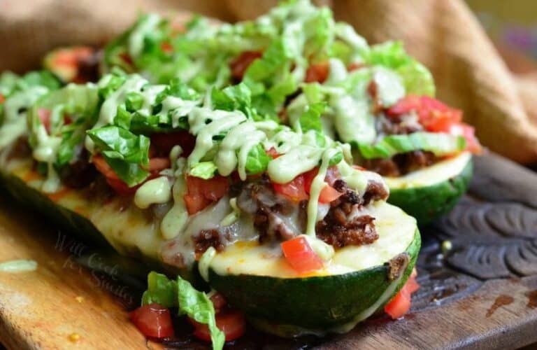 two stuffed zucchini boats with beef, lettuce, and avocado dressing.