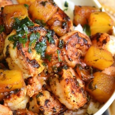 a white bowl filled with white rice and sauteed shrimp and pineapple over it.