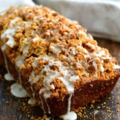 Zucchini bread with glaze on top on a wood cutting board.