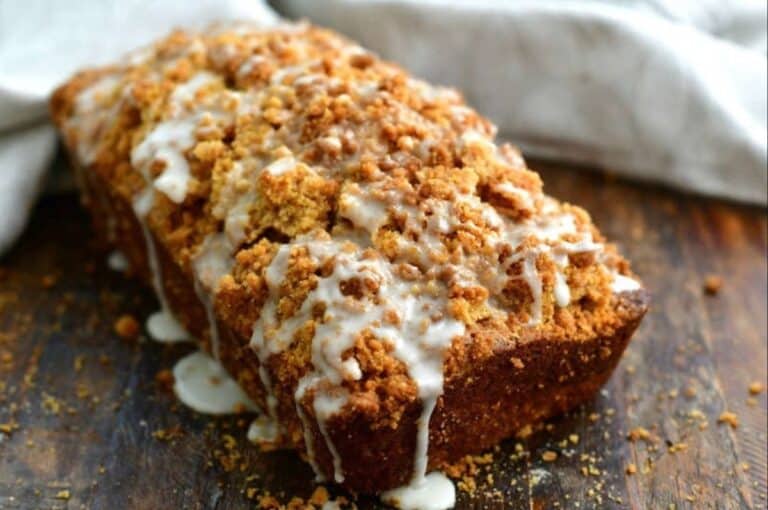 Zucchini bread with glaze on top on a wood cutting board.