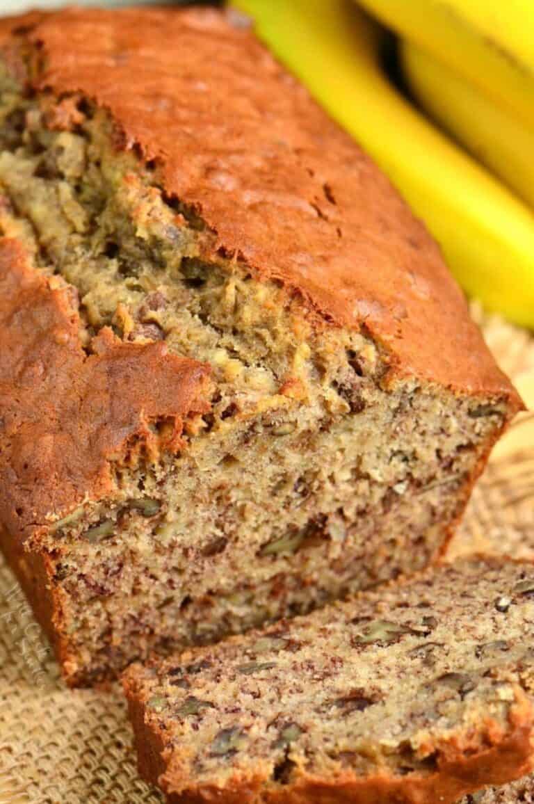 banana bread with a slice out of it laying on a burlap placemat.