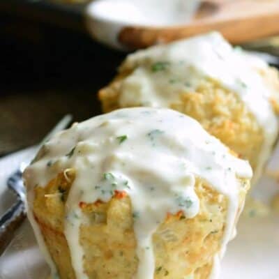 two garlic parmesan chicken meatloaves on a white plate with white sauce over them.