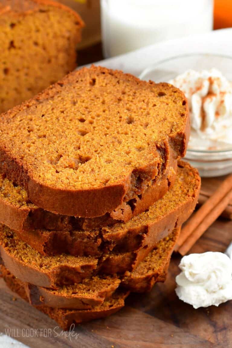 pumpkin bread slices stacked up and whipped cream on a spoon next to it.