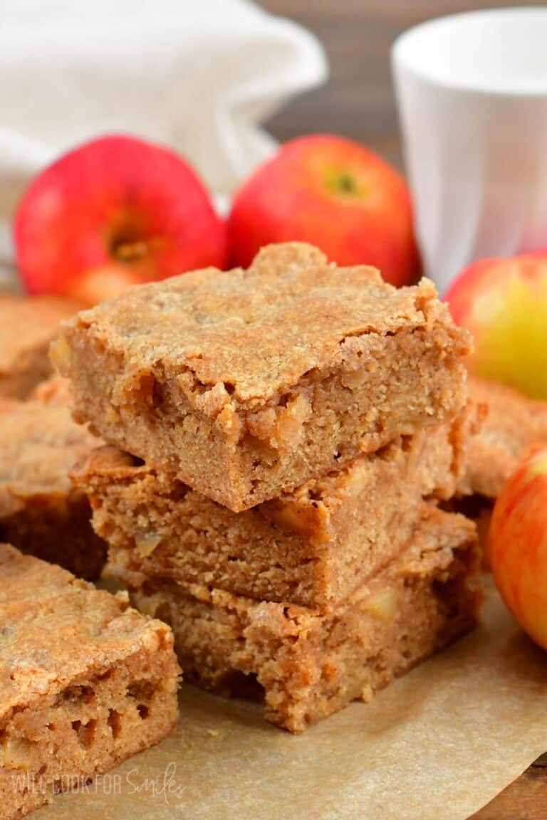 Apple pie blondies stacked up on wax paper with apples in the background.