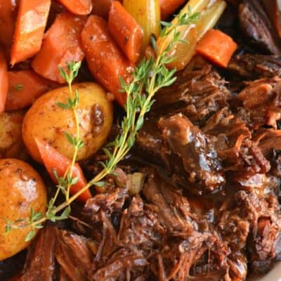 Pot roast with carrots and potatoes and a sprig of thyme in a bowl.