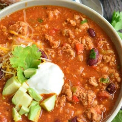 chili in a bowl with sour cream, avocado, and cilantro on a wood surface.