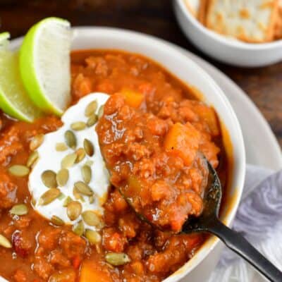 pumpkin chili in a bowl with a spoon scooping some out and pumpkin seeds as garnish.