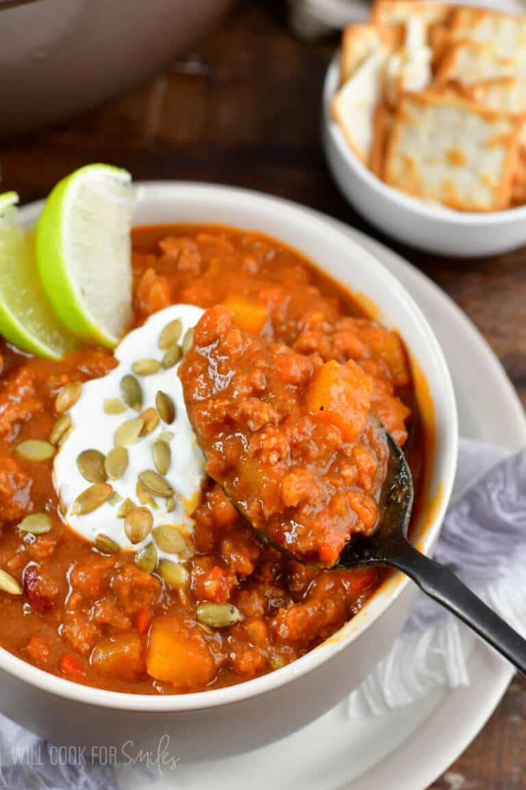 pumpkin chili in a bowl with a spoon scooping some out and pumpkin seeds as garnish.