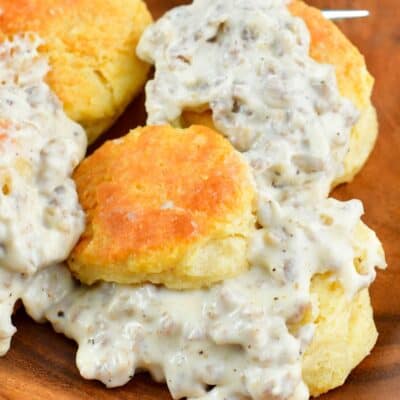 plate with several biscuits with sausage gravy over them on a wood plate.