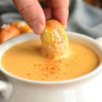 dipping a pretzel bite into the beer cheese dip in a bowl.