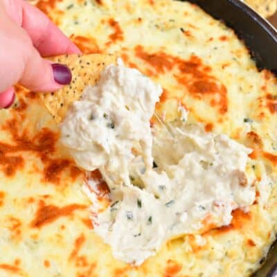 scooping out some creamy chicken dip from the skillet with a tortilla chip.