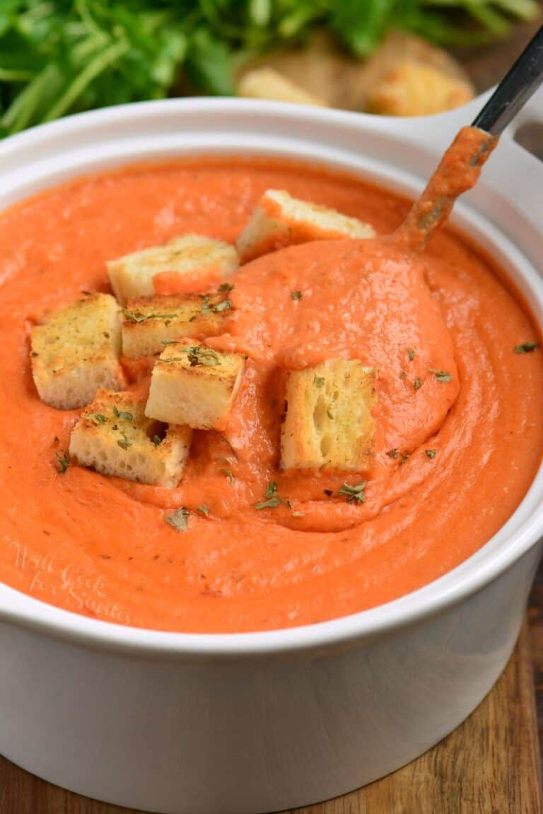 tomato bisque in a bowl with croutons on top and a spoon scooping some up.