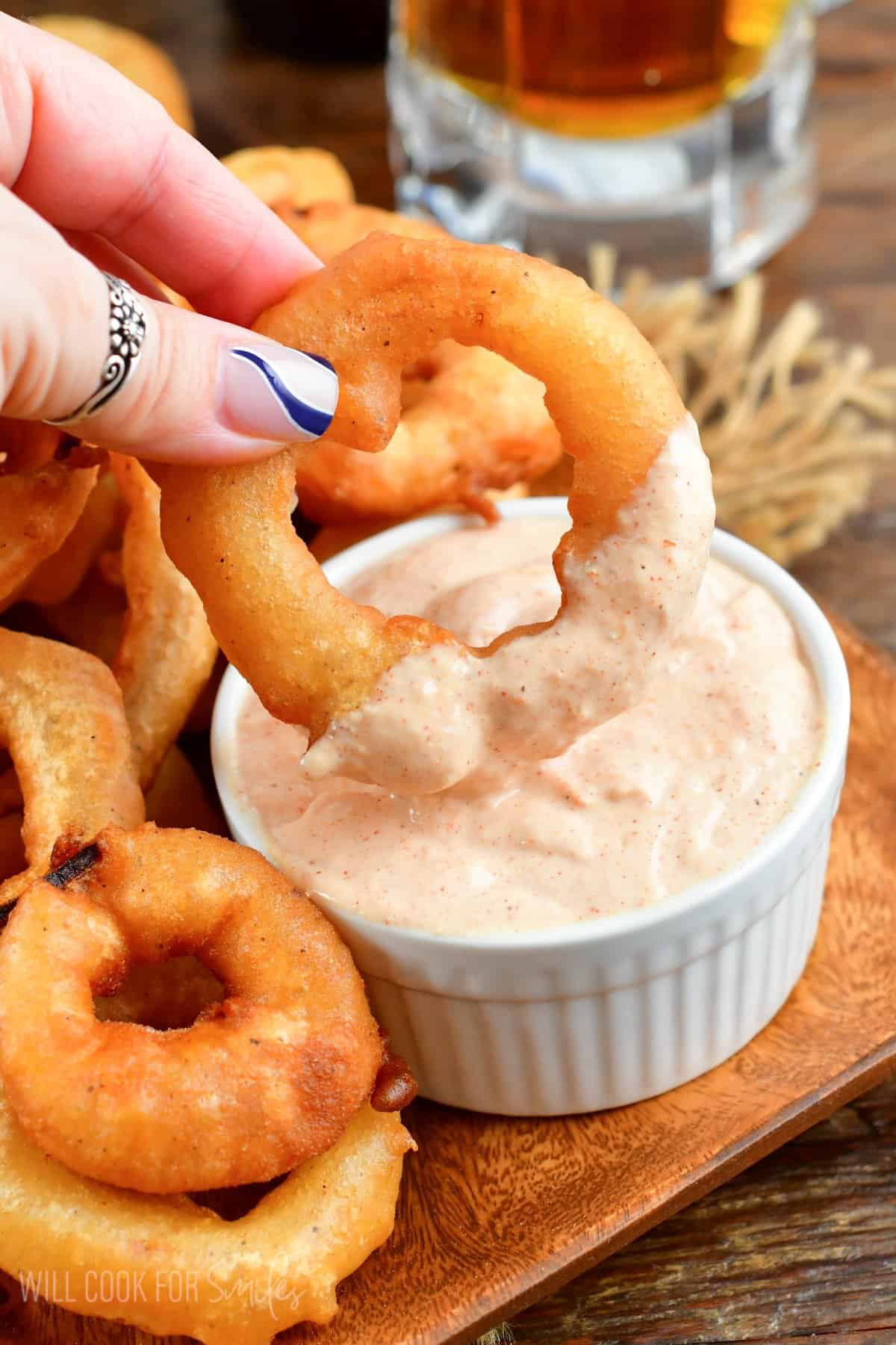 Beer battered onion ring being dopped into sauce that is in a small bowl.