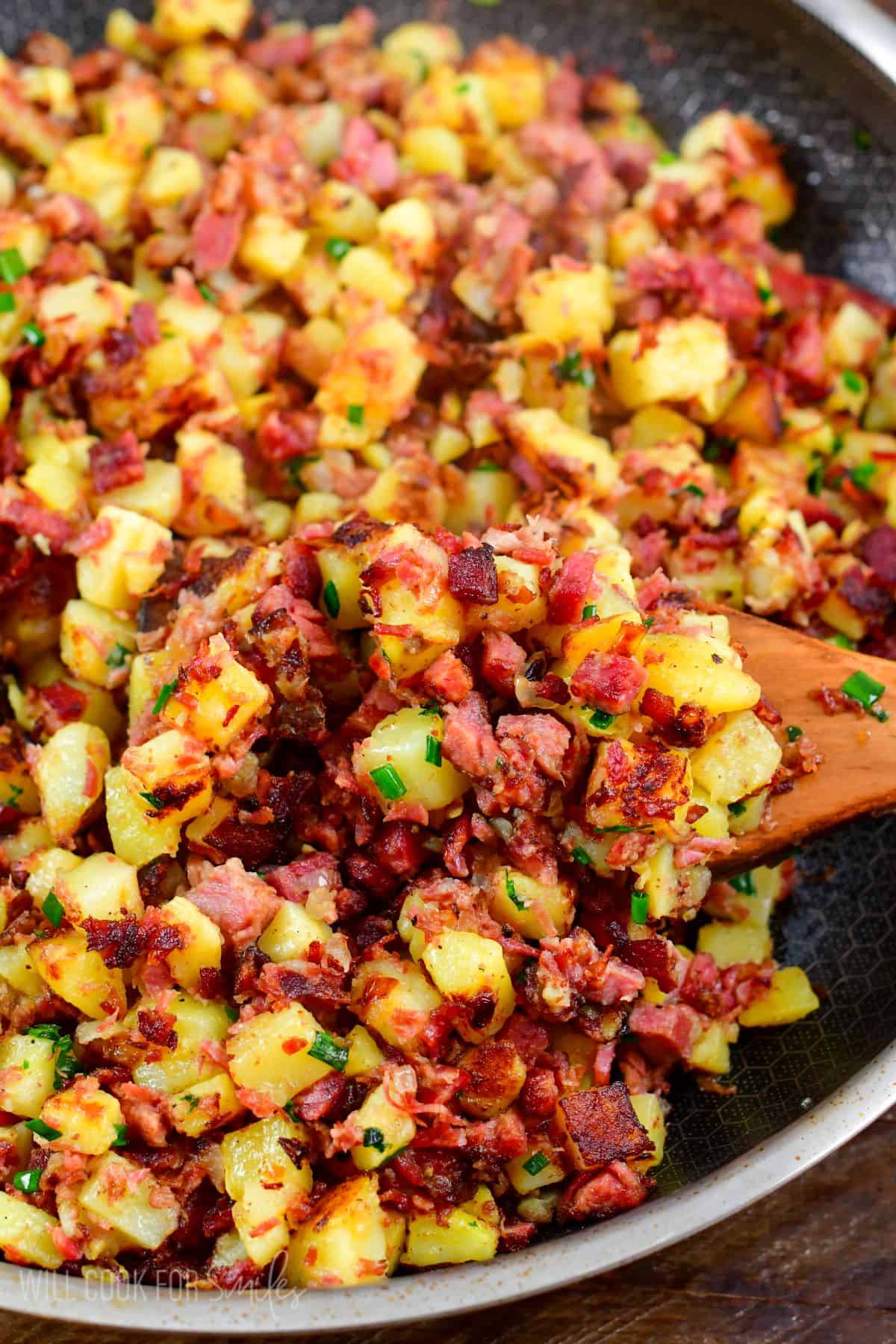 Corned beef hash in a pn with a wooden spatchula scooping some up.