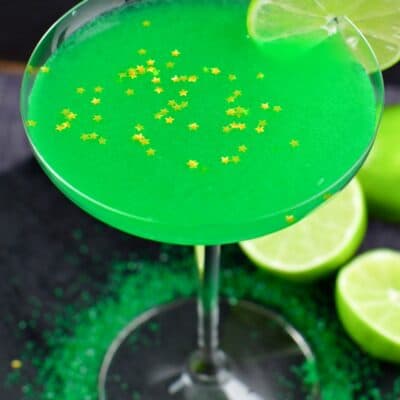 Lime martini in a martini glas with a lime on the edge of the glass and gold stars sprinkles on top.