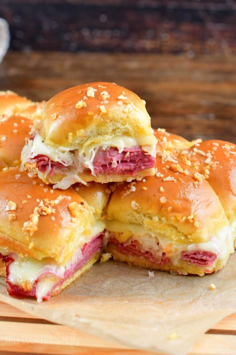 Rueben sliders staked on parchment paper on a cutting board.