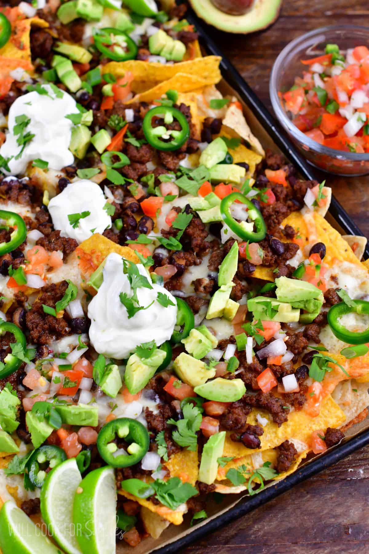 Beef nachos on a baking sheet on a wood surface.