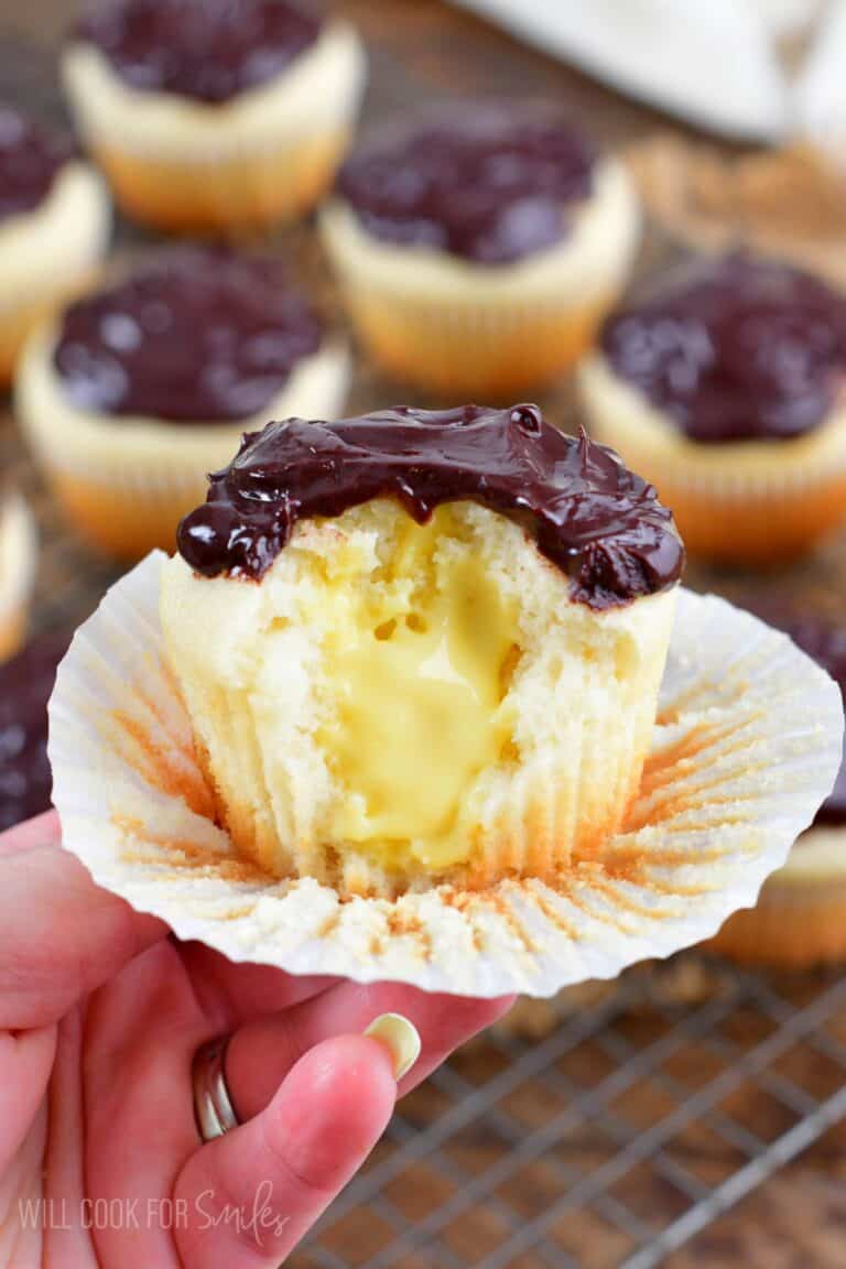 Holding a Boston cream cupcake with a bite taken out of it.