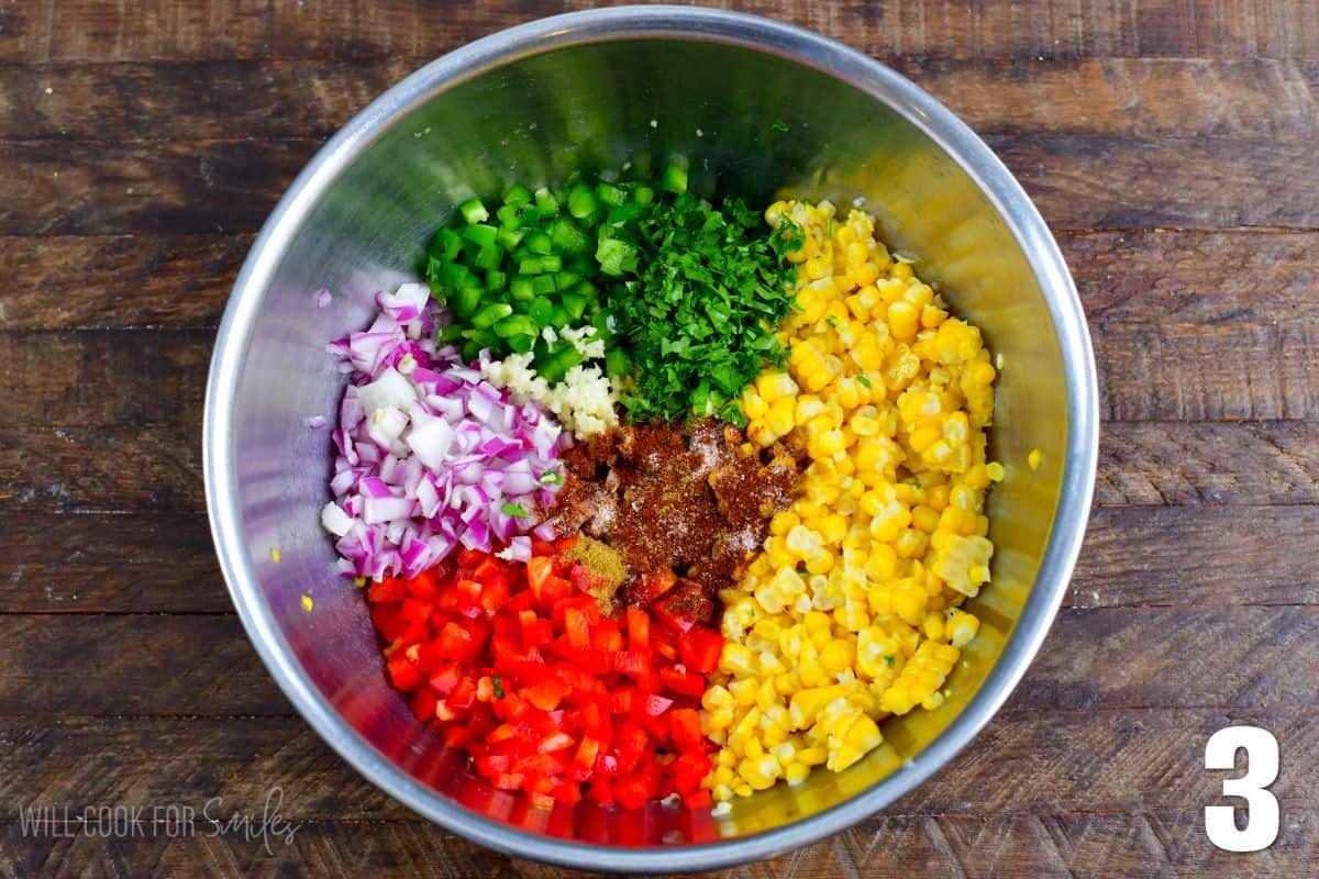 the ingredients for corn salsa in a metal bowl on a wood surface.