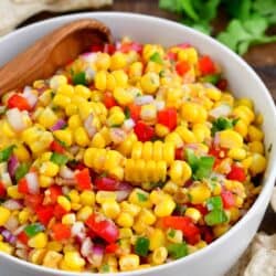Corn salsa in a white bowl with a wooden spoon sitting in the bowl.