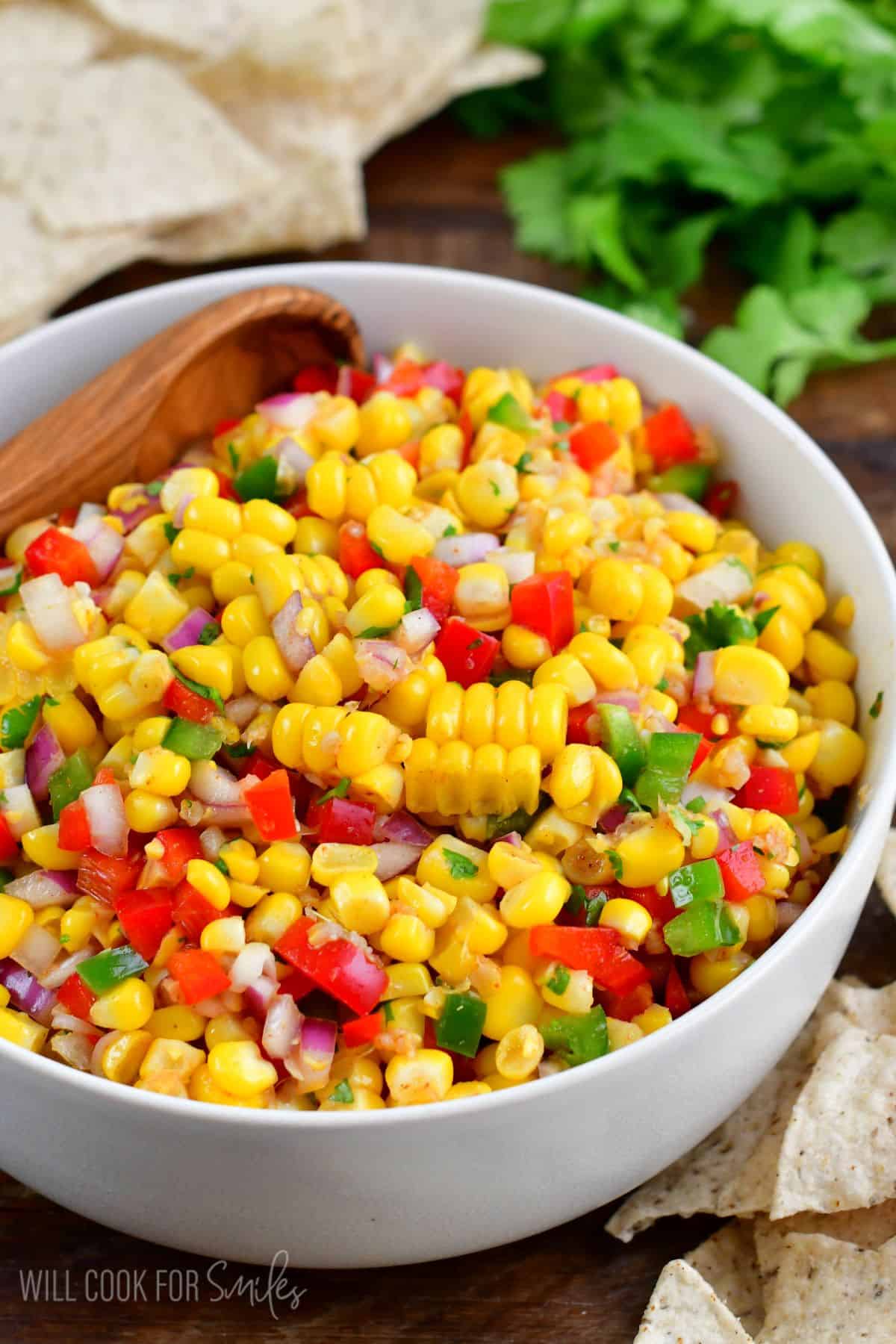 Corn salsa in a white bowl with a wooden spoon sitting in the bowl.