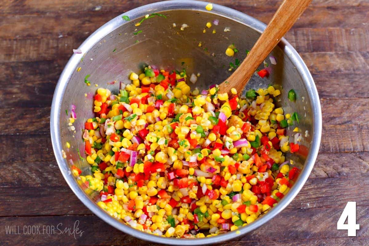 Mixing corn salsa in metal bowl with a wooden spoon.