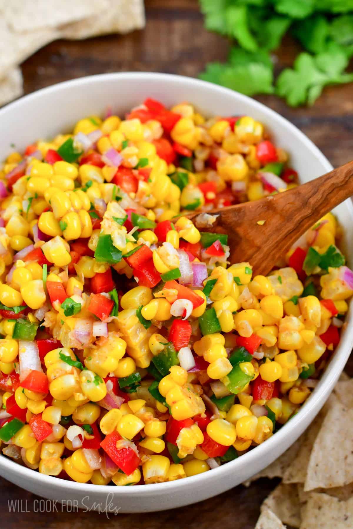 Scooping corn salsa up with a wooden spoon out of a white bowl.