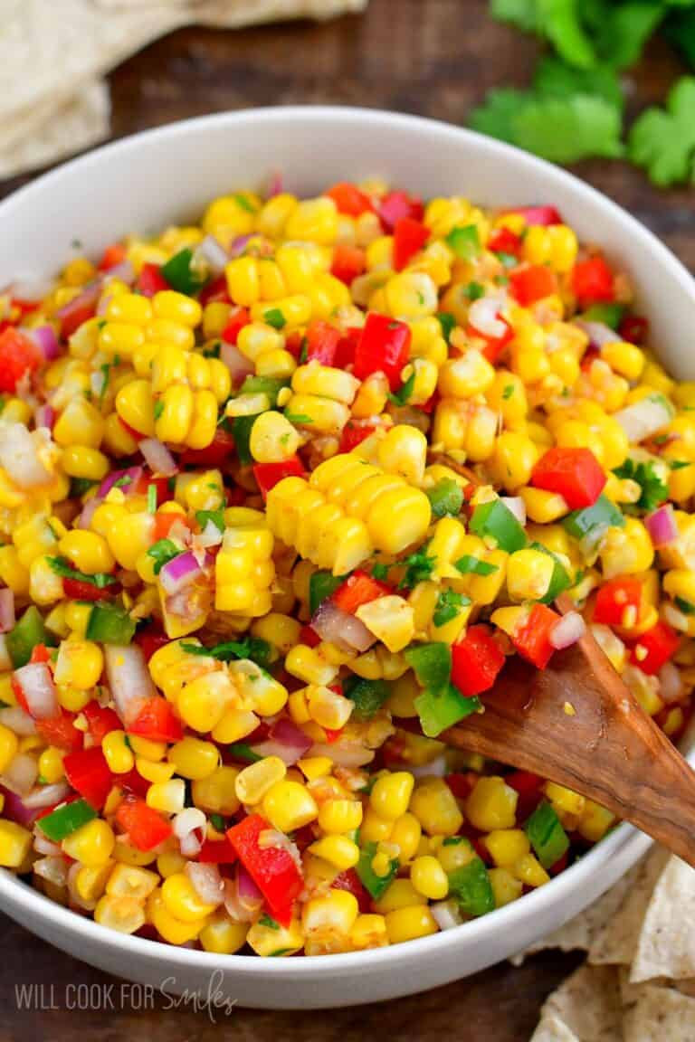 Corn salsa in a white bowl scooping some up with a wooden spoon.