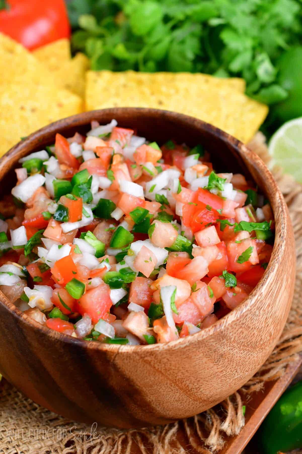 Pico de Gallo in a wood bowl on a burlap placemat.