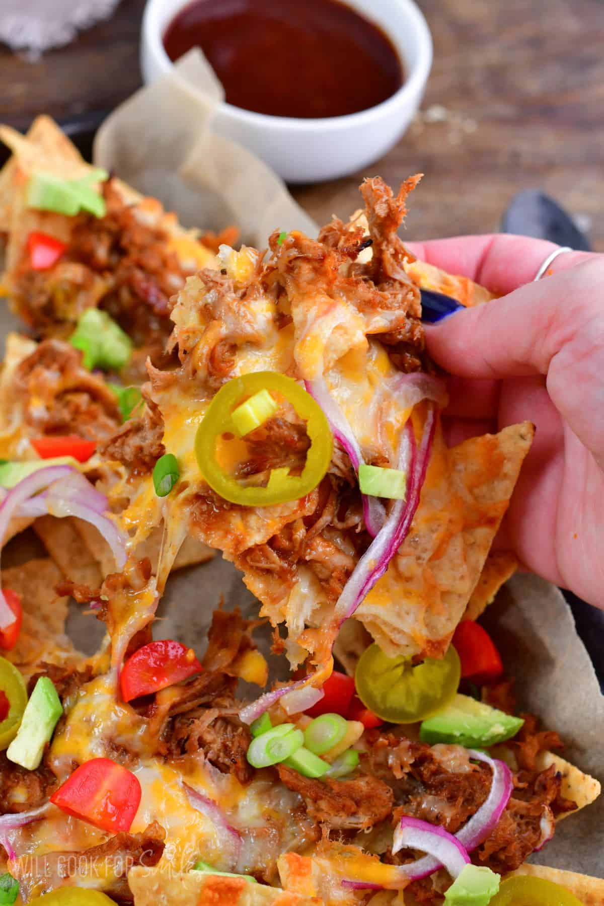 Pulled pork nachos on a baking sheet and pulling some of the nacho out.