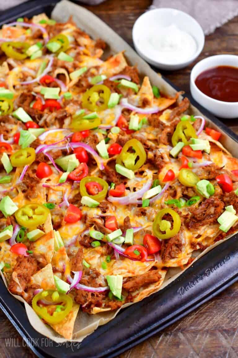 Pulled pork nachos with all the toppings and sour cream in a small bowls to the side.