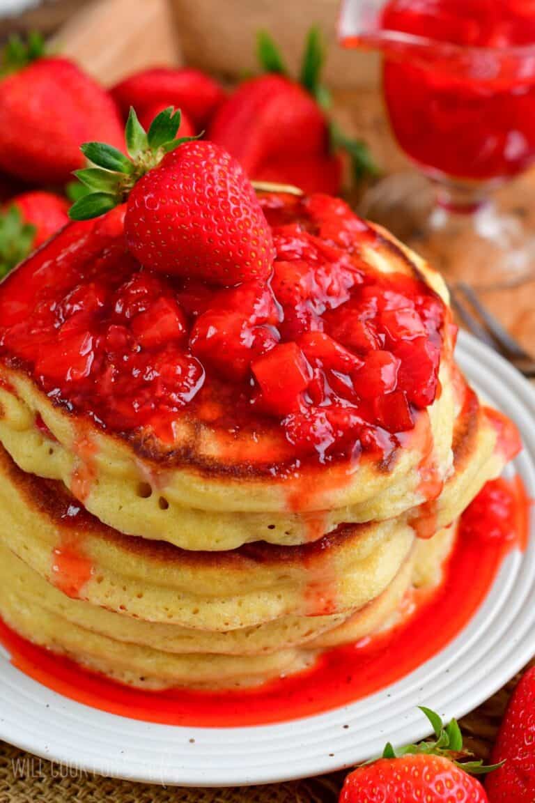 strawberry pancakes with strawberry topping and a whole strawberry on top.